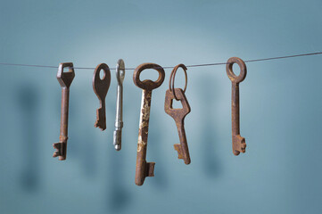 A different old retro rusty keys from different locks hanging on string with a drop shadow on a blue wall