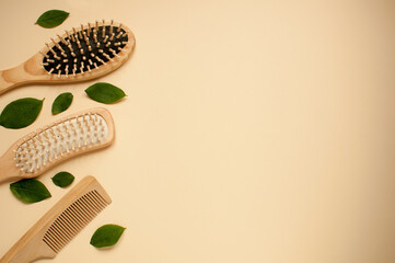 Fototapeta premium three wooden combs and green leaves on a beige background with space for text