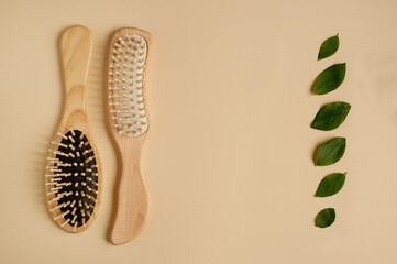 two massage wooden combs and green leaves in the form of a vertical row on a beige background with space for text