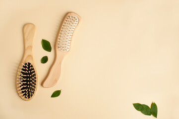 two massage wooden combs and a few green leaves in a row on a beige background with space for text