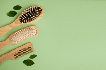 three massage wooden combs and a few green leaves on a green background with space for text