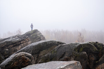 A traveler stands on the top of a mountain in a rocky park and watches the fog. A wonderful moment of the miracle of nature.