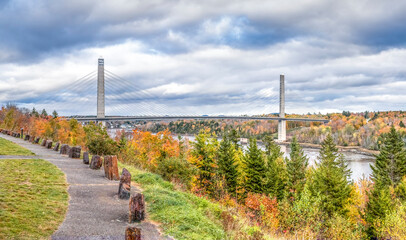 The Penobscot Narrows Bridge spans the Penobscot River near Bucksport, Maine surrounded by colorful fall foliage on a cloudy autumn day. - 466189343