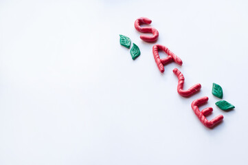 the word sale is made of plasticine red letters with white inclusions, arranged diagonally, on a white background with a place for the text and green plasticine leaves