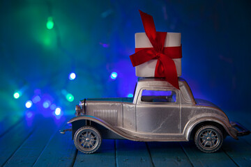 Retro car with a gift on the roof against the background of Christmas lights.