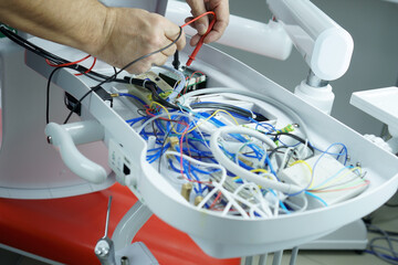 The master checks the electrical circuit in the faulty dental chair with a tester device. Repair of medical equipment.