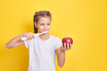 beautiful brown-haired teenager girl brushes her teeth with an electric toothbrush on a yellow background