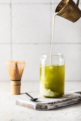 Green matcha tea with milk in a transparent glass on a light background.