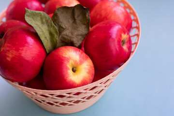 Close up basket full of ripe juicy red apples on blue background. Organic garden fruits