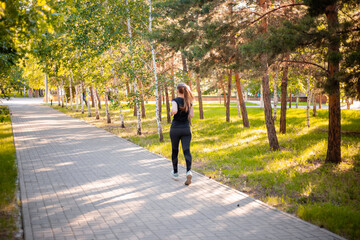 Back view a girl in a black sports uniform is jogging in the evening park. Self-sports concept. 