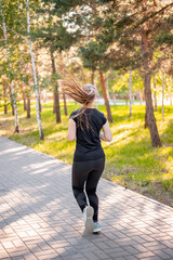 Back view a girl in a black sports uniform is jogging in the evening park. Self-sports concept. 