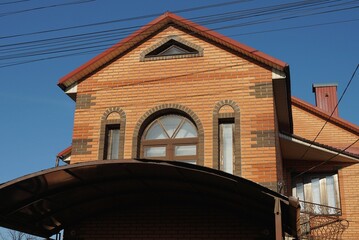 the attic of a red big brick house with windows under a brown tiled roof against a blue sky