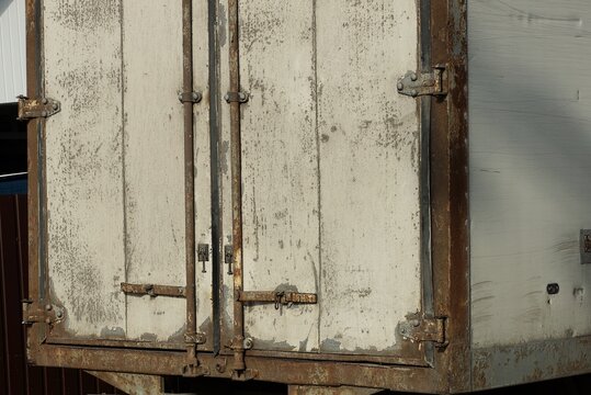 part of an  gray dirty old metal booth with a closed door on a truck on the street