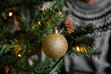 Bola dorada brillante de navidad con luces y persona de fondo