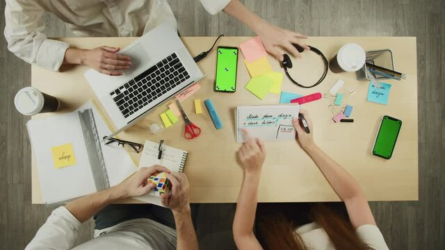 Business people working in modern office together top view. Creative workers discussing tasks. Project planning, group brainstorming. Team leader in headphones typing on laptop keyboard.