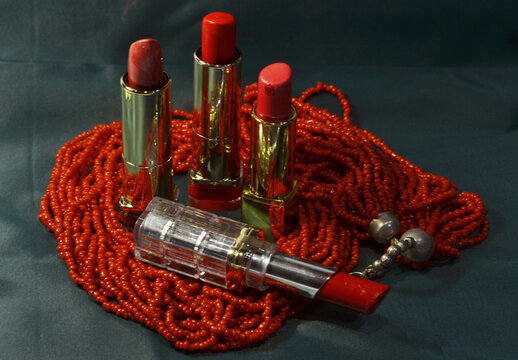 Different shades of red lipstick with coral beads on a dark background
