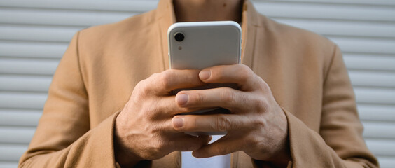 Cropped view of smartphone in hands of man in brown coat outdoors, banner 