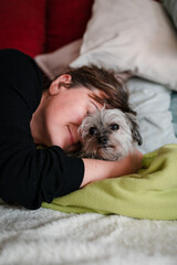 Female pet owner hugging her lapdog lying on couch. Love of a human and a dog.
