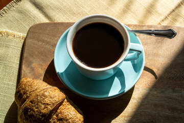 Cup of coffee and croissant ,illuminated by sunlight , autumn day.