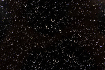 Closeup Of Water Drops Falling On Window In Rainy Weather At Night. Abstract View On Black Background Through Glass Covered With Condensation.