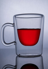 Transparent glass coffee cup with red pomegranate juice, isolated on bright reflective background