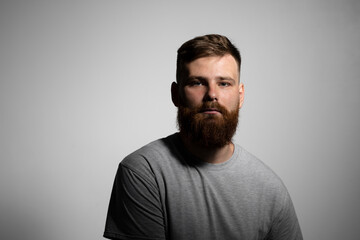 Close-up portrait of a handsome a brunette brutal bearded man in a grey t-shirt. Stylish and handsome man with a beard.