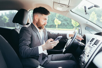 Male businessman sitting behind the wheel of a car, frustrated can not understand the steering and instructions funky car, reads additional information from the phone