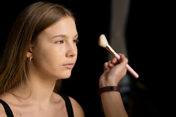 Fototapeta premium Professional make-up artist working with brush on model face. Process of making makeup. Portrait of young blonde woman in beauty salon interior. Applying tone to skin.
