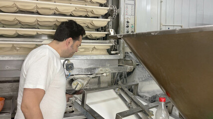 Pending baker on his factory's bread-making machines. Baker making bread in his small business machines. Concept bread, baker, factory, business, bakery, artisan.