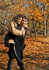 Happy young couple has fun in the autumn park. Young woman and man walking outdoors.