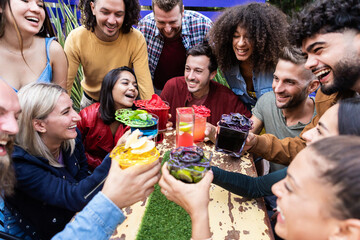Group party of friends cheering with trendy and multicoloured drinks at fashion cocktail bar - Young people gathering and celebrating together - Youth lifestyle concept - Focus on caucasian man