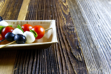 Close up on aperitif snacks of tomatoes, olives, mozzarella and basil on wooden background with copy space