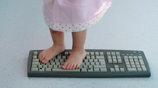 child stands, jumps, dances with his feet on computer keyboard, presses buttons, little vandal, bully plays with gadget, bullying concept, spoils technology until parents can see