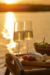 Amazing sunset on the lake, white wine, fruit cake, apples, grapes, brie cheese, biscuits. Autumn aesthetic picnic.