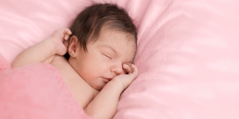 Fototapeta na wymiar Cute newborn baby is in a pink blanket sleeps sweetly, covering one eye by hand. Face of newborn girl is close-up with place for text