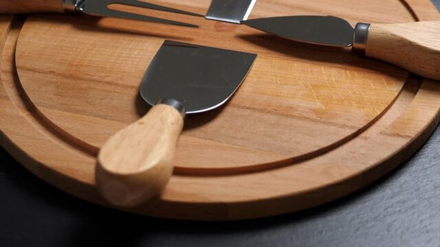 Cheese knifes and fork on wooden platter. Rotating