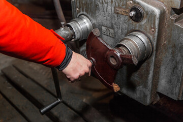 The hand of a man in a red work suit, holds on to the handle and controls the work of an old milling machine in an industrial plant