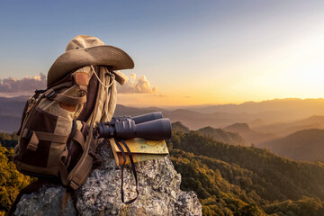 Binocular with map paper and hiker hat and backpack on top of rock mountain at sunset