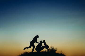Obraz na płótnie Canvas silhouette of a happy family with a child at sunset against the sky, father kisses little daughter.