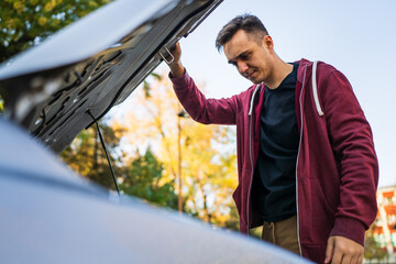 Adult caucasian man standing by his car checking failed engine of broken vehicle