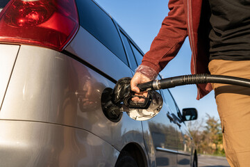 Close up on hand of unknown caucasian man hold black gas pump nozzle pouring gasoline into the fuel...