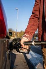 Close up on hand of unknown caucasian man hold black gas pump nozzle pouring gasoline into the fuel tank refueling petroleum to vehicle at self service petrol station during crisis copy space