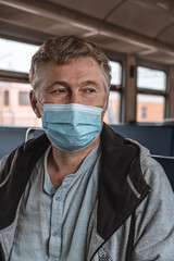 Fototapeta na wymiar Portrait of a serious adult man with a medical protective mask on his face inside a public transport. Social distance during the coronavirus pandemic. Preventive measure. Disease protection concept.