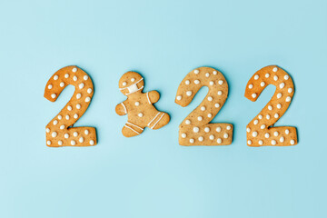 Happy New Year's set of numbers 2022, gingerbread man in face mask from ginger biscuits glazed sugar icing decoration on blue background, minimal seasonal pandemic winter holiday card