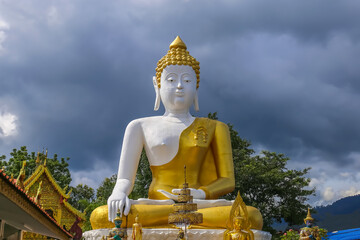 Fototapeta premium Beautiful big buddha image with rain cloud sky at Wat Phra That Doi Kham. Chiang Mai, Thailand.