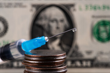Needle of a disposable syringe with a drop of liquid on the tip against the background of a fragment of a US dollar bill