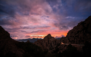 Fototapeta na wymiar Sunrise over the Calanches of Piana in Corsica with lightning in the distance and car lights passing along the D81 road