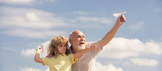 Grandson child and grandfather playing with paper plane against summer sky background. Child boy with dreams of flying or traveling.