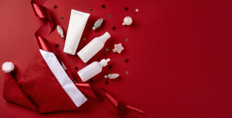 White bottles cosmetic products with red ribbon and Christmas decoration on red background....
