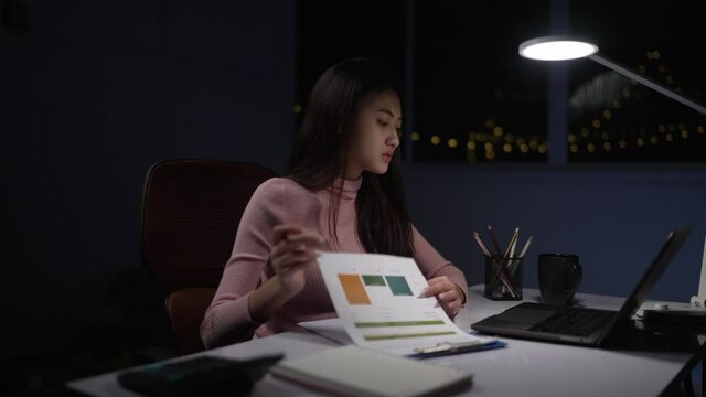 Asian woman freelance career wearing pink clothes doing paperwork There is a laptop on the table. and lanterns lit up, deliberately staying at home during Welsh at night